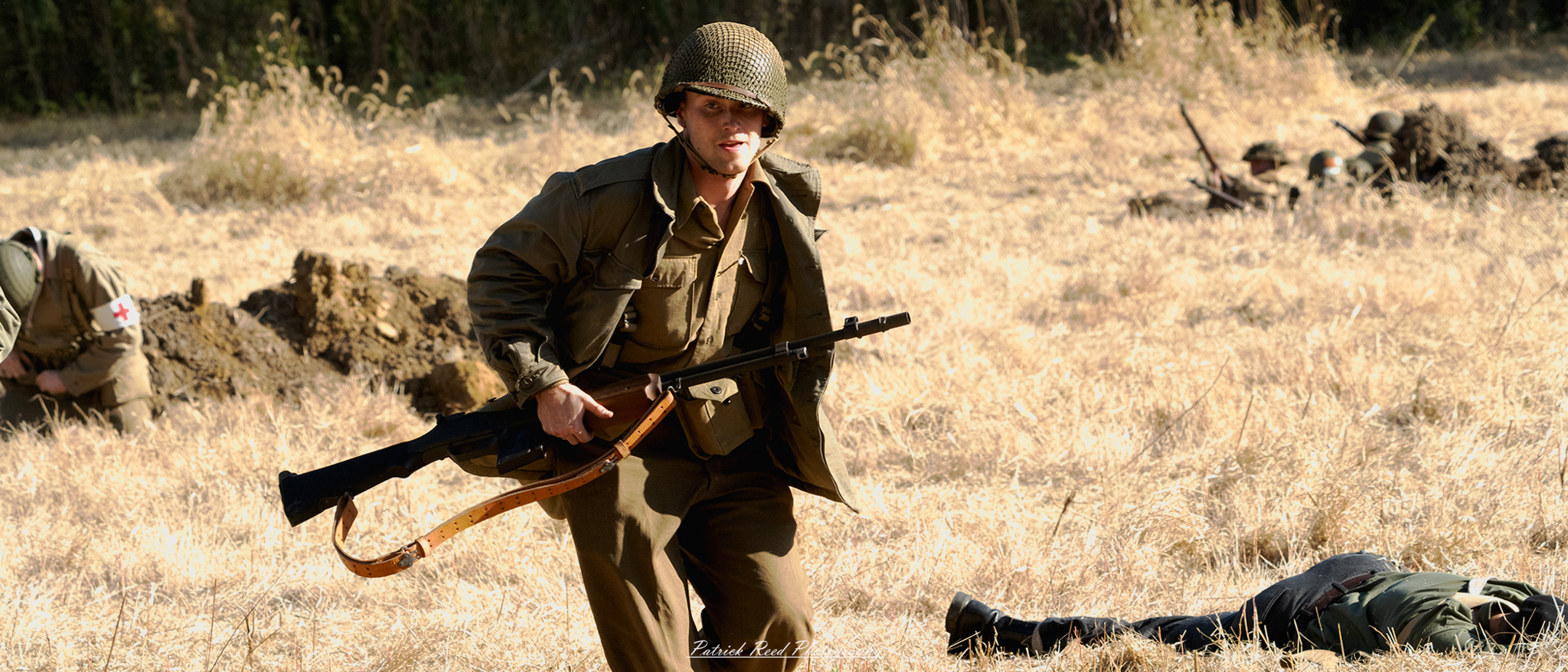 "Image of a soldier sprinting through an open field while carrying a Browning Automatic Rifle (BAR). The soldier is clad in a WWII-era uniform, showcasing determination and urgency as he navigates the terrain. Dust and grass kick up around him, capturing the intensity of movement. The background reveals a blurred landscape of greenery and distant trees, emphasizing the soldier's focus and speed. This action shot highlights the bravery and dynamic nature of combat."